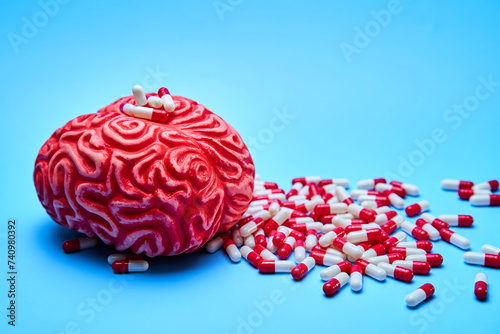 Representation of a red brain with a pile of red and white pills on a blue surface. Concept of addictions. photo