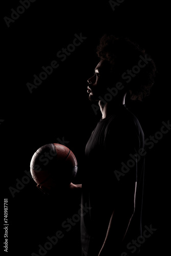 Basketball player holding a ball. Concentrated african american sports man against black background. © Nikola Spasenoski