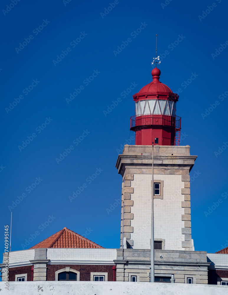 The red tower of the lighthouse against the bright blue sky, low angle view.