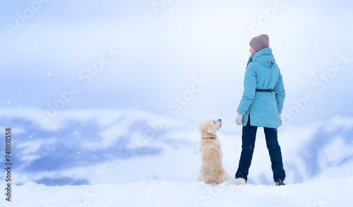 Golden retriever sits near owner and looks devotedly at her owner in a blue jacket in the winter mountains. Holidays in the mountains in winter photo