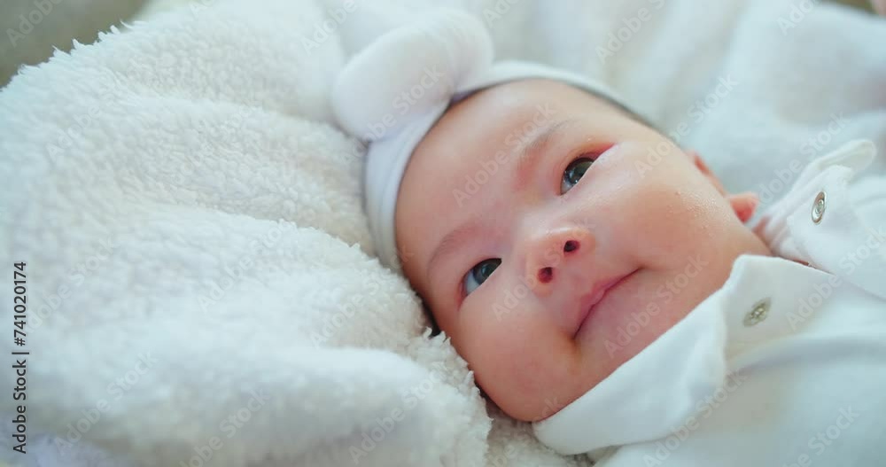 A contented baby with sparkling eyes and a soft headband lies on a plush fluffy white blanket, exuding warmth innocence and comfort A contented baby with sparkling eyes and a soft headband lies on a plush fluffy white blanket, exuding warmth innocence and comfort