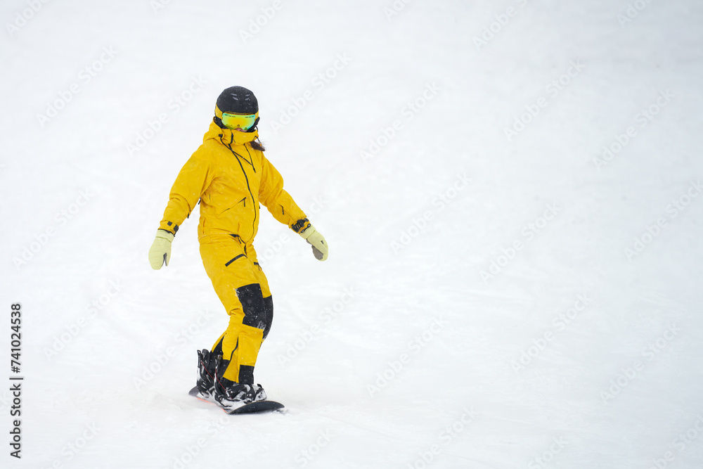 Girl snowboarder rolling down a snowy slope. Copy space.