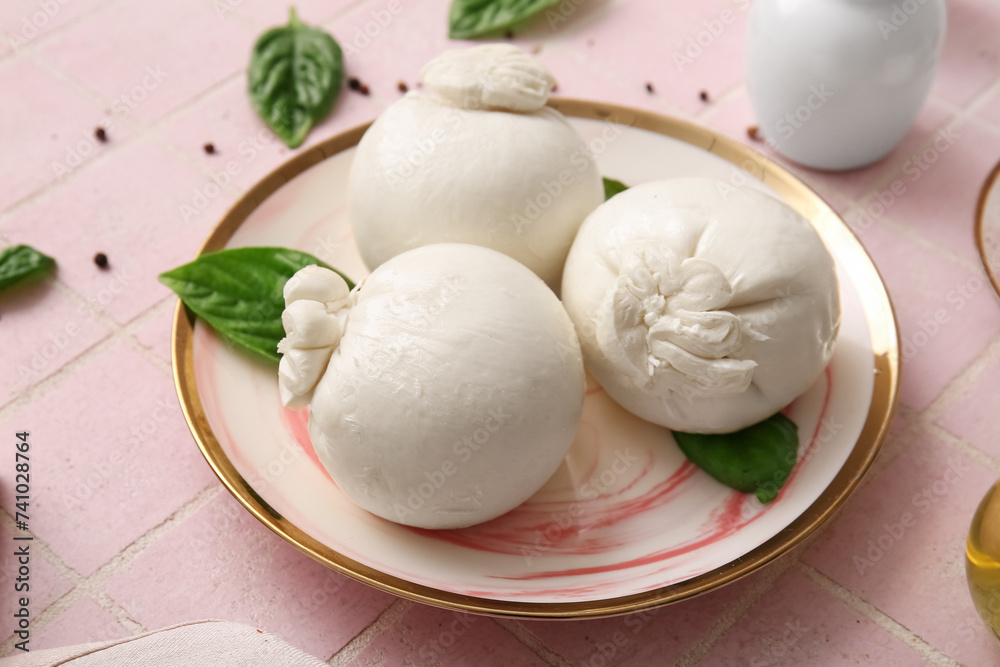 Plate of tasty Burrata cheese with basil on pink tile table Plate of tasty Burrata cheese with basil on pink tile table