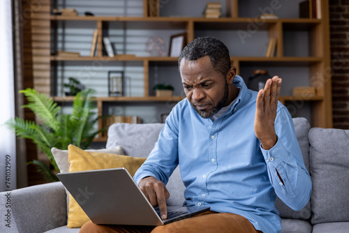 Frustrated african american man with laptop having technical difficulties at home
