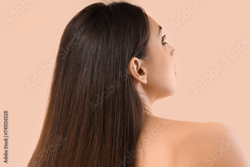 Young brunette woman with beautiful hair on beige background, back view