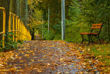 Alone wooden bench standing in park next to sidewalk with long yellow railing next to street