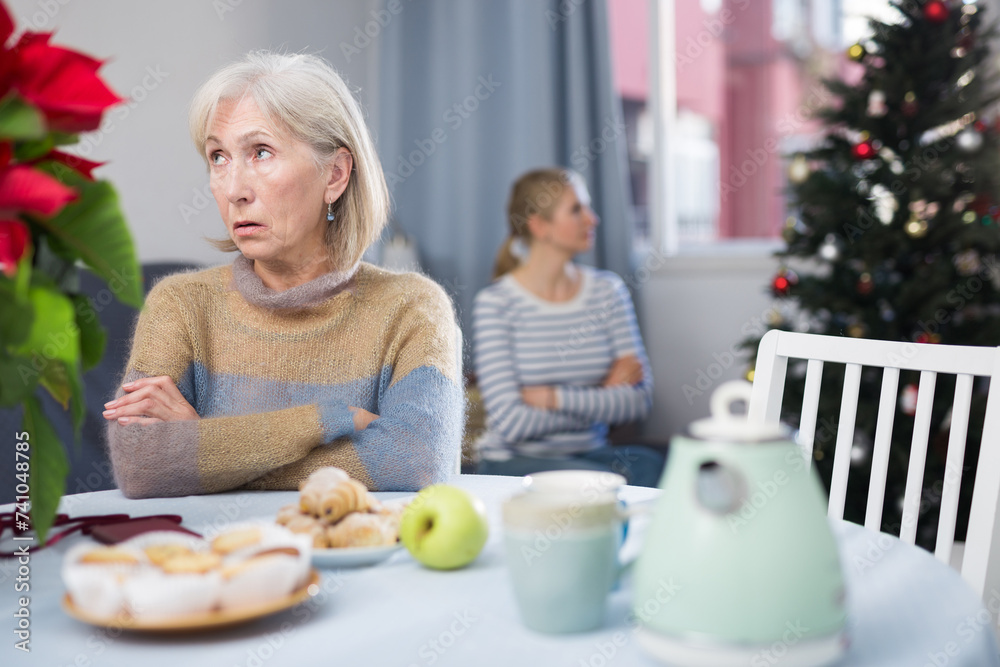 Mature woman, sitting at a table, and her adult daughter were very offended at each other after a quarrel