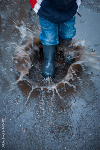 A child plays in a puddle - steps into a water with force and splashes fly away. Vertical image, motion blur, slight unsharpness. photo