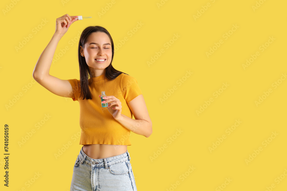 Young woman with remedy for hair loss treatment on yellow background