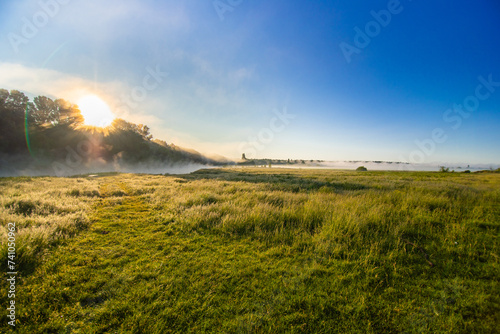Landscape with sunrise from behind the forest over the river with fog.