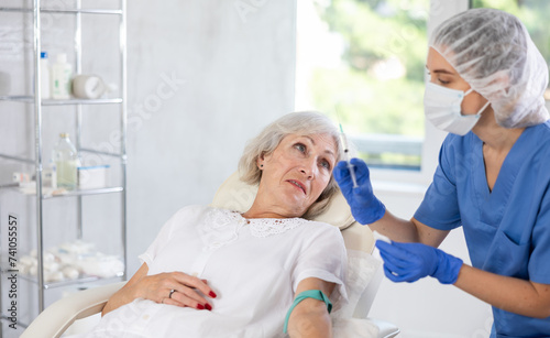 Old gray haired lady laying at examination couch before having intravenously injection by nurse