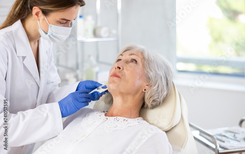 Professional young doctor in scrub giving senior female patient smile line fillers.