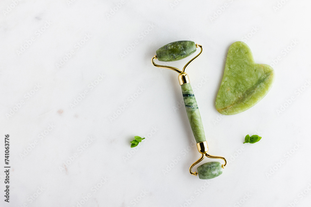 Green jade roller massager for face on white marble. Green jade roller massager for face on white marble.