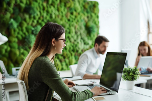young woman is working at laptop in modern office with a living green vertical wall of moss,concept of sustainable development, caring for planet, climate change, increasing oxygen levels, air quality © Наталья Лазарева
