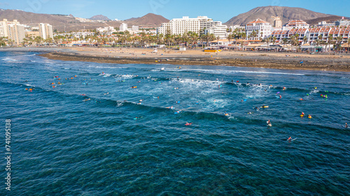 Aerial photo from drone to de surfers in the ocean beachs Adeje Playa de las Americas, Playa Honda In the background Tenerife at sunset. Tenerife, Canary islands, Spain