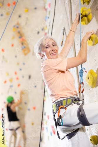 positive muscular woman under guidance of trainer overcomes difficult climbing route in gym.