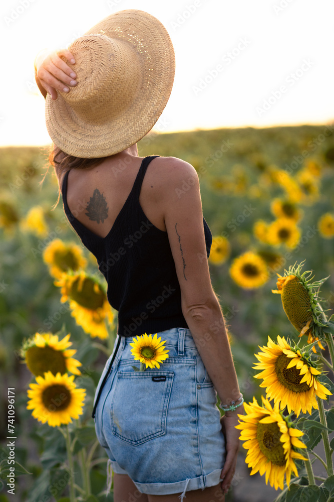 Young woman on her back in a sunflower plantation during golden hour