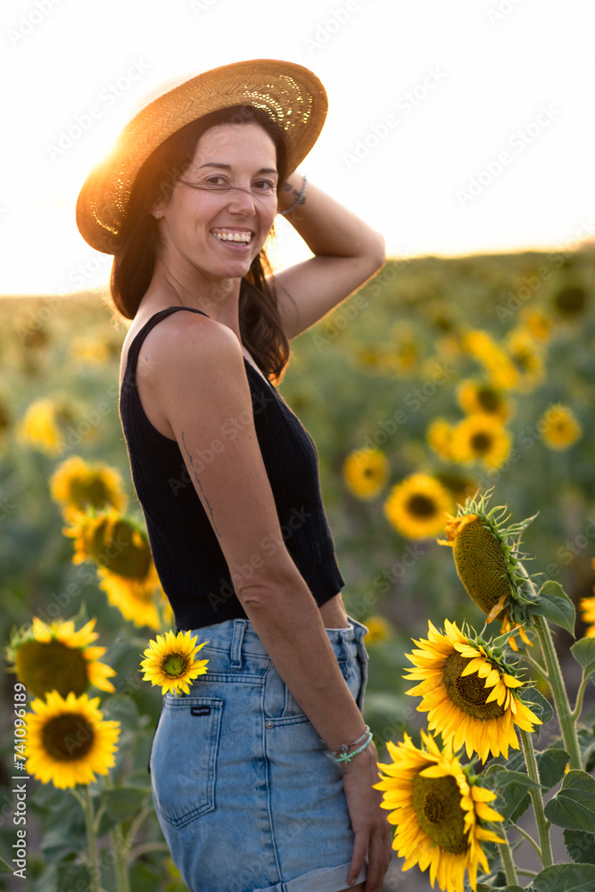 Young woman from behind looking at camera in a sunflower plantation during golden hour
