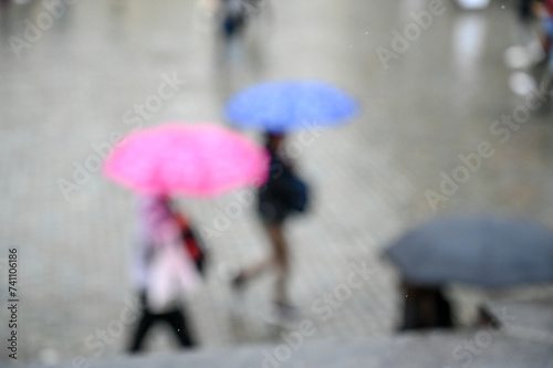 Blurred photo of people with umbrella walking in the city on rainy day. Rain falling. 
