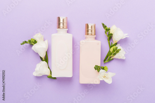 Facial cosmetic products with freesia flowers on color background, top view