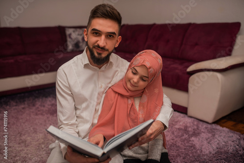 Happy Muslim famliy at home, young father and child daughter together reading a Quran during Ramdan photo