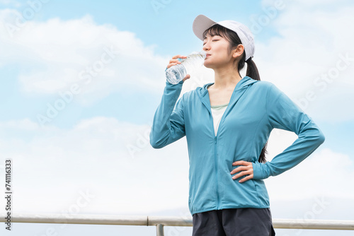 ウォーキング・ジョギング・運動中に水・スポーツドリンクで水分補給するアジア人女性 