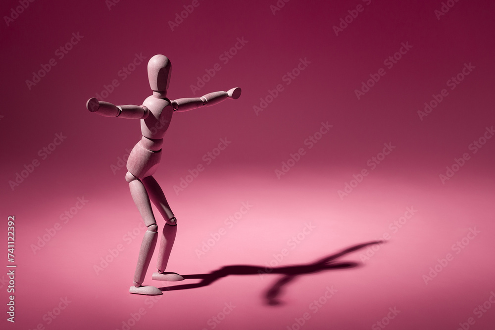 A wooden mannequin posing with arms outstretched on a pink background A wooden mannequin posing with arms outstretched on a pink background