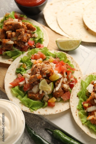 Delicious tacos with vegetables, meat and lime on grey textured table
