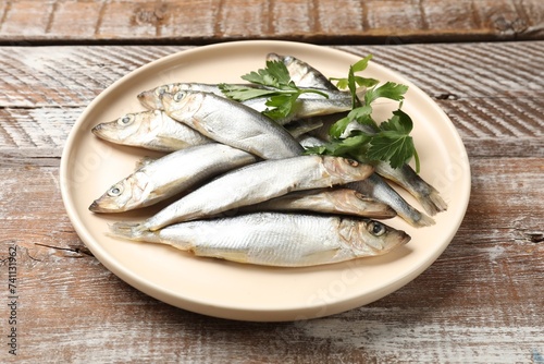 Fresh raw sprats and parsley on wooden table, closeup
