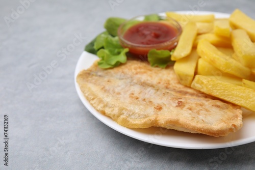 Delicious fish and chips with ketchup and lettuce on gray table, closeup. Space for text
