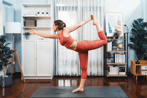 Flexible and dexterity woman in sportswear doing yoga position in meditation posture on exercising mat at home. Healthy gaiety home yoga lifestyle with peaceful mind and serenity.