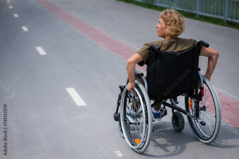 Rear view of an elderly woman in a wheelchair riding on a bike path. Rear view of an elderly woman in a wheelchair riding on a bike path.