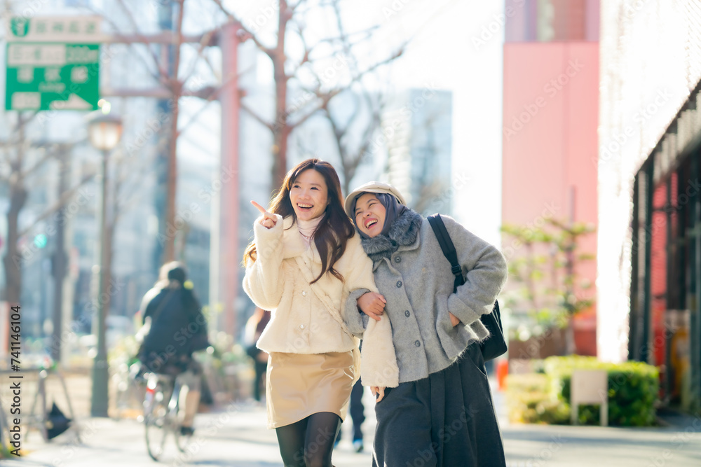 Fototapeta premium Travel, woman girl tourist Two Asian friends but different religions, one of whom is a Muslim girl. Walking tour of the city, city view, traveling in Japan. with fun She is traveling in the city area.