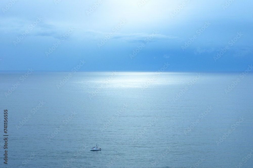Sunlight reflecting off the ocean on a clear day with a fishing ship in the foreground. 