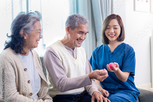 Senior couple get medical service visit from caregiver nurse while using round squishy ball for muscle strength in pension retirement center for rehabilitation and longevity post recovery process photo