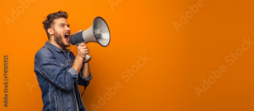 A man shouting through megaphone portrait in the studio orange background.

 photo