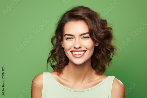 Portrait of a cheerful young woman with curly hair, smiling on a green background.