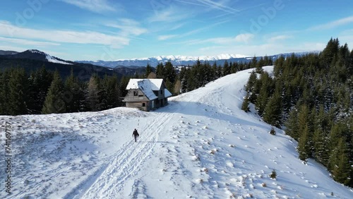 Drone shot of a hiker walking on a snowy trail by a wooden hut in Bucegi Mountains in BrasovRomania photo