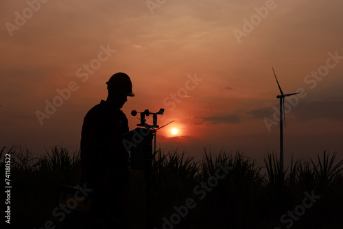Silhouette of young men engineer standing checking equipment wind turbine beside agricultural sugarcane and wind turbine morning sunlight
