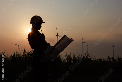Silhouette of young female engineer holding a blueprint standing beside agricultural sugarcane and wind turbine morning sun star light effect background,.. © SHUTTER DIN
