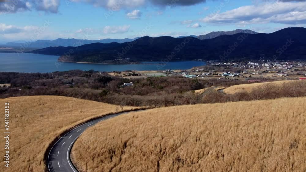 Winding road through golden fields with a lake view and mountains in the distance, aerial shot Winding road through golden fields with a lake view and mountains in the distance, aerial shot