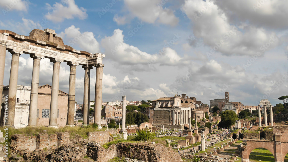 A view of the Roman Forum ruins, with the Basilica of Maxentius in the background, under a partly cloudy sky.