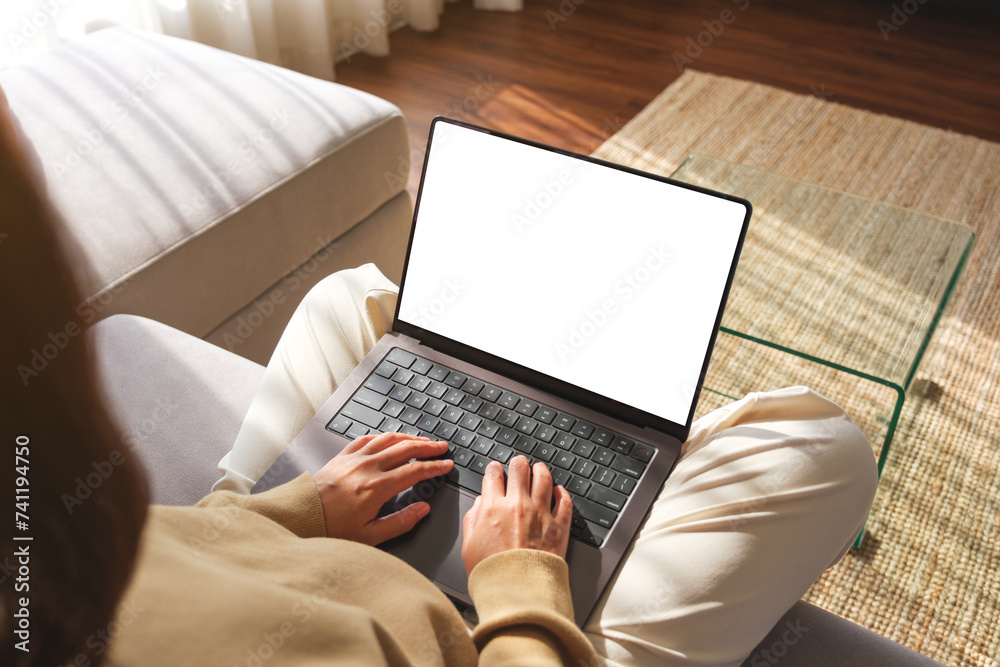 Fototapeta premium Mockup image of a woman working and typing on laptop computer with blank screen while sitting on sofa at home