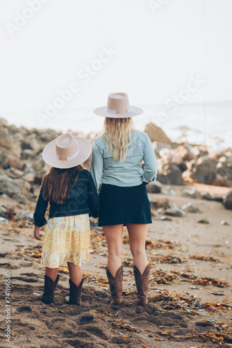 Woman and her daughter in cowboy boots and skirts at the beach wearing pink cowboy hats