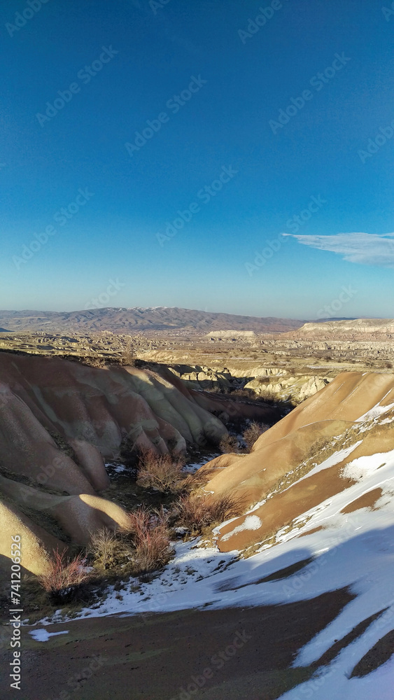 A panoramic view of a snowy landscape with rock formations and clear blue sky.