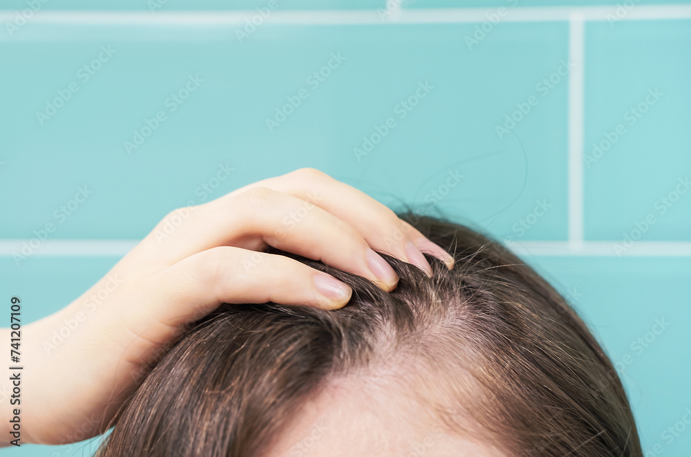 Fototapeta premium Woman touching her hair close-up on against background of mint tiles, hair loss concept.