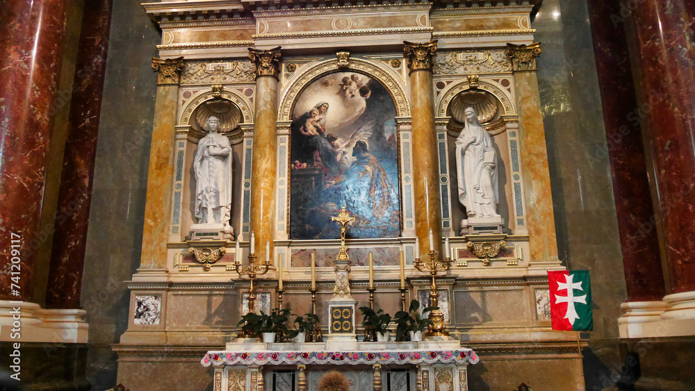 An ornate altar with religious artwork and statues, adorned with flowers, under a vaulted ceiling. An emergency exit sign is visible.