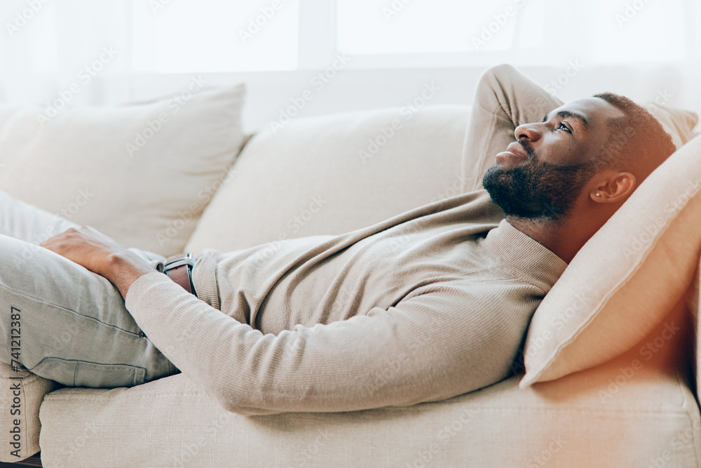 Relaxing at Home on the Weekend Smiling African American Man Sitting on a Comfortable Sofa in the Living Room, Holding a Tablet and Enjoying Modern Technology With a Background of a Cozy and Stylish Relaxing at Home on the Weekend Smiling African American Man Sitting on a Comfortable Sofa in the Living Room, Holding a Tablet and Enjoying Modern Technology With a Background of a Cozy and Stylish
