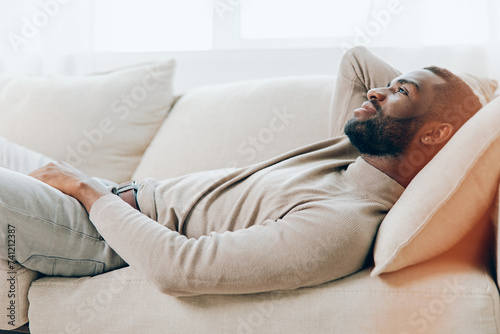 Relaxing at Home on the Weekend Smiling African American Man Sitting on a Comfortable Sofa in the Living Room, Holding a Tablet and Enjoying Modern Technology With a Background of a Cozy and Stylish