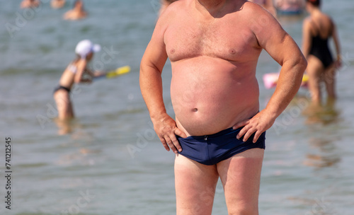 Fototapeta Naklejka Na Ścianę i Meble -  Fat man in swimming trunks on the sea beach